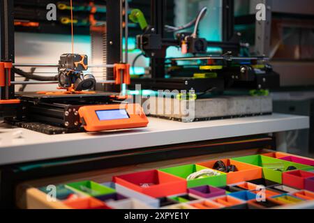 Home studio. 3D printers at work. Production, passion and hobby. Orange plactic filament. Drawer with printed elements. Order in the studio. Stock Photo
