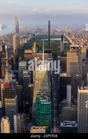 Aerial Helicopter Photo Over Central Park with Nature, Trees, People Having Picnic and Resting on a Field Around Manhattan Skyscrapers Cityscape. Beautiful Evening with Warm Sunset Light Stock Photo