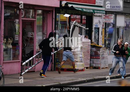 People remove a new artwork by Banksy, depicting a howling wolf painted on a satellite dish that was placed on a shop roof in Peckham, south London. The artist's latest artwork comes a day after he unveiled three monkeys painted on a bridge in Brick Lane, east London. Picture date: Thursday August 8, 2024. Stock Photo