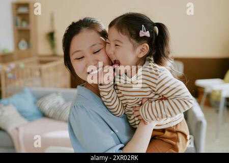 High angle portrait of Asian mother and her daughter hugging while little girl biting her point finger Stock Photo