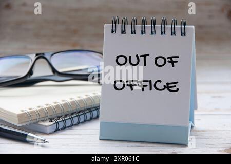Out of office text on white notepad with notes and glasses background. Stock Photo
