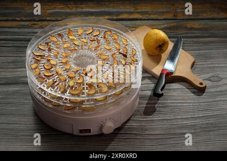 dried apple slices on a drying rack and a knife with whole apple ready to prepare Stock Photo
