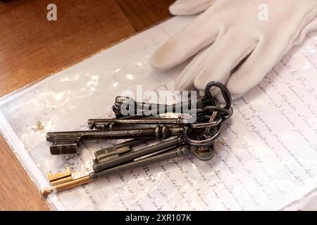 A close-up shot of an antique key bundle resting on an old handwritten document with a white gloved hand in the background. Stock Photo