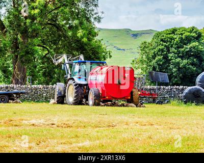 A tractor in a lush green field, preparing to roll hay bales under a clear blue sky. Stock Photo