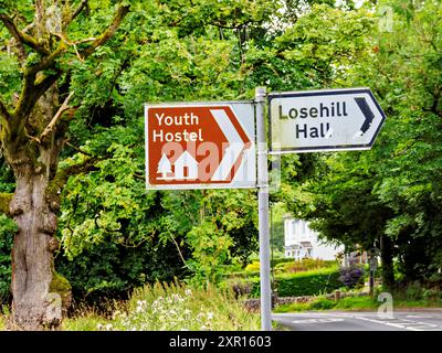 Guide signs point to a youth hostel and Losehill Hall amidst a scenic rural landscape with lush trees. Stock Photo