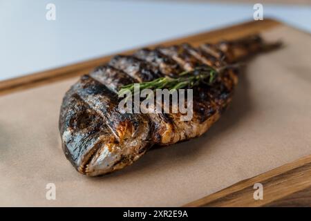Dorado fish baked with lemon and rosemary on a barbecue on a wooden board Stock Photo