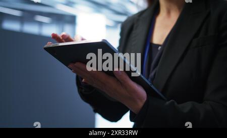 Programmer managing data center with advanced technology using digital device. Close up shot of woman walking in server room, optimizing data center tech with tablet, camera B Stock Photo