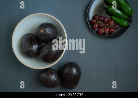 Three avocados in a bowl and two on a gray table. Stock Photo