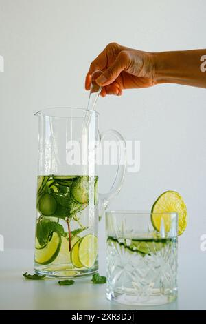 Woman's hand mixing detox water with cucumber and lime in a cocktail steer Stock Photo