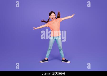 Full size photo of little girl spread hands fly surfing keep balance dance wear trendy red outfit isolated on purple color background Stock Photo