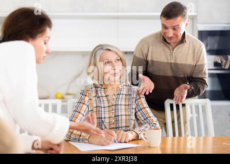 Old woman compiling heritage document while middle-aged man and woman ...