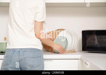 Young woman putting dishes near microwave on counter in kitchen Stock Photo