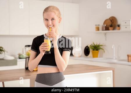 Happy sporty young woman drinking healthy smoothie in kitchen Stock Photo