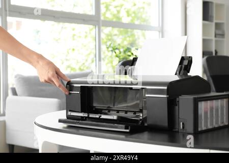 Female hands putting paper sheet in modern printer on table in stylish office Stock Photo