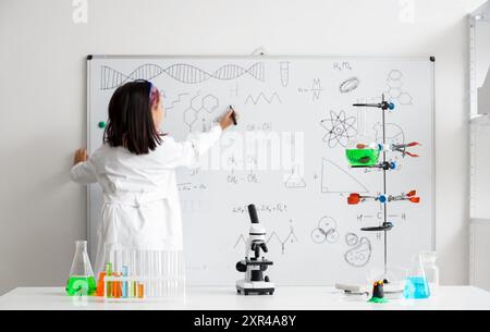 Cute little girl writing on whiteboard at chemistry lesson in classroom Stock Photo