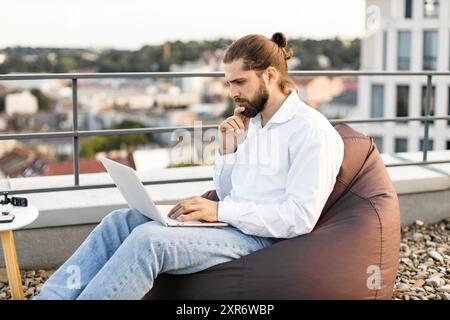 Man working on laptop outdoors with city view in background Stock Photo