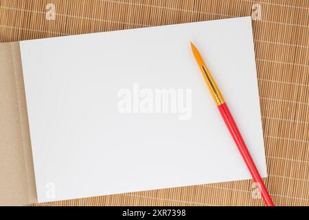 close up of paint brush and sketch book for aquarelle laying on bamboo mat Stock Photo