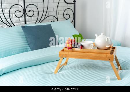 Wooden Breakfast Tray With Teapot, Grapes, and Cup on a Blue Bed Stock Photo