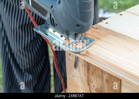 A hobbyist DIY carpenter cutting a plank of wood with a jigsaw - a type of power tool with a reciprocating blade Stock Photo