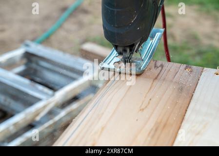 A hobbyist DIY carpenter cutting a plank of wood with a jigsaw - a type of power tool with a reciprocating blade Stock Photo