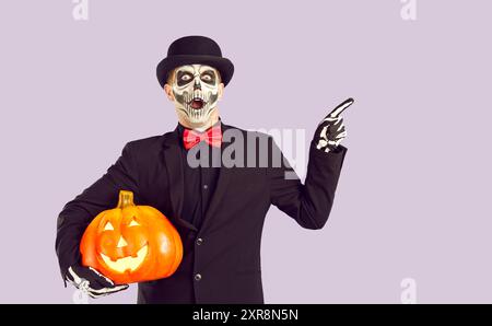 Shocked man dressed in Day of the Dead costume points his finger to side on light lilac background Stock Photo