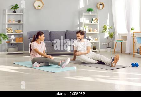 Couple sitting on the floor on yoga mat and talking after doing sport fit exercises at home. Stock Photo