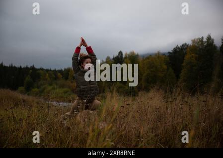 Woman Practicing Yoga Poses in a Serene Autumn Landscape Near a River Stock Photo