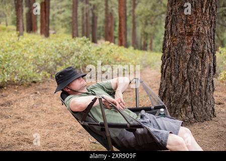 Man resting in a camping chair in the woods Stock Photo