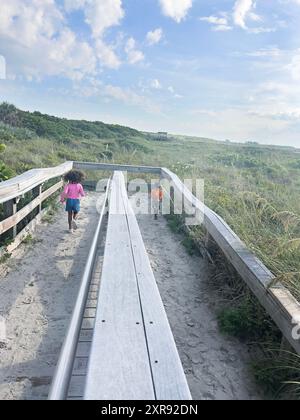 Two children running on a wooden boardwalk and sand path through Stock Photo