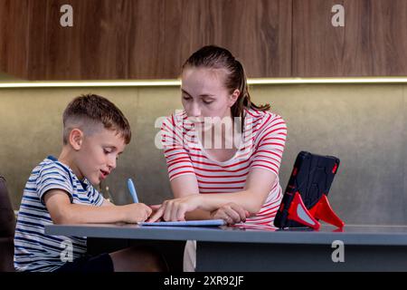Beautiful mother helping son doing schoolwork at home Stock Photo