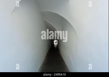 Dark narrow white corridor with people silhouettes at the end Stock Photo