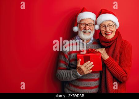 Christmas banner granparents in a santa hat holding a gift on a red background with place with copyspace Stock Photo