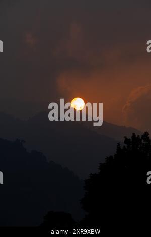 A stunning dawn featuring an orange sun and sky setting over the layered mountains in Chamba, Himachal Pradesh, India. Stock Photo