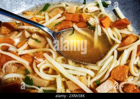 Noodle soup, strong beef broth with carrot, spoon, closeup. Stock Photo