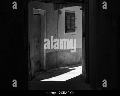 Cres, Croatia - October 23, 2022: Narrow street in Cres sunlight and shadow, black and white Stock Photo