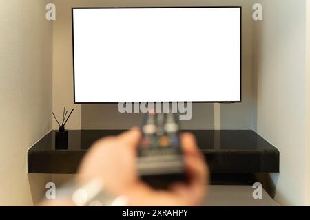 A person is relaxing on a sofa while holding a remote control in front of a flat-screen television. White screen, clipping path. Stock Photo