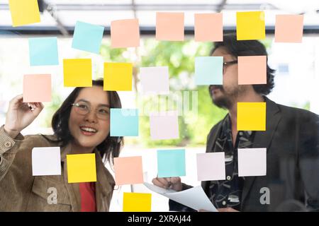 Business people meeting at office and using post notes to share ideas, brainstorming ideas, sticky notes on glass wall. Business people reading adhesi Stock Photo