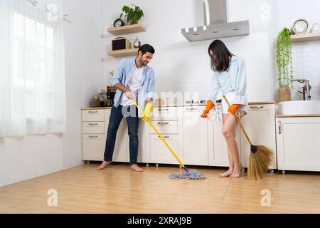 Happy couple cleaning kitchen together and looking at each other. Happy young couple having fun while doing cleaning at home. Stock Photo