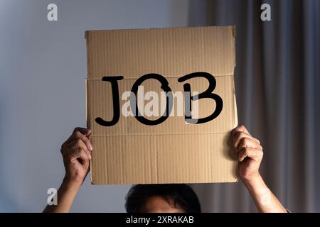 Business man holds up a cardboard sign with the words job. A man holding a cardboard with an inscription needs a job. Concept of job search, a reducti Stock Photo