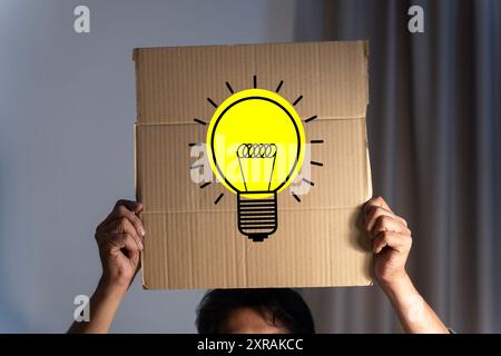 Conceptual image of businessman gesturing with a cardboard box on his head with light bulb. Businessman holding a sign with light bulb, concept of the Stock Photo