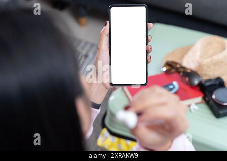 Smartphone with blank empty screen copy space in female hands, clipping path. Woman with white wireless earbud in ear using mobile phone for listening Stock Photo