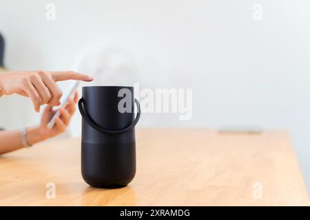 Close-up on hand using phone connecting portable speaker. Women connecting mobile phone to wireless portable speaker on table.  Hands connecting cell Stock Photo