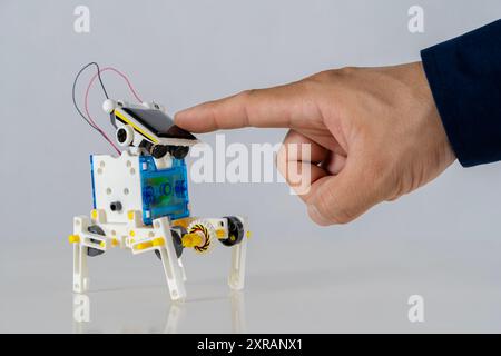 A finger touches a solar panel above a toy robot made from plastic packaging. Sustainable technology education concept. Learning in innovation, new th Stock Photo