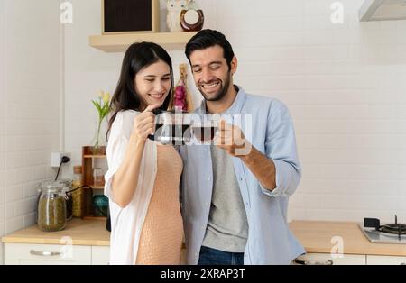Cheerful biracial young couple enjoying coffee and talking while standing in kitchen, copy space. Happy young couple have fun in modern kitchen indoor Stock Photo
