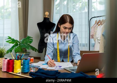 Female designer of clothes standing by sewing machine in atelier, attractive tailor after work stand posing, looking at camera smiling. female use mea Stock Photo