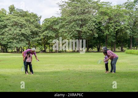 Grandparents explained to granddaughter playing badminton that the park has trees and beautiful green grass as a place to relax in the family. Stock Photo