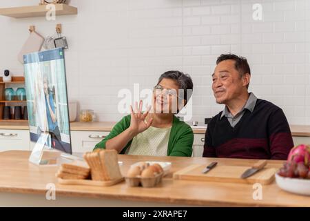 Gray-haired man and woman video calling relatives using laptop, sitting at table communicating with elderly friends. virtual communication sitting in Stock Photo