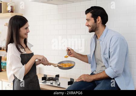 Happy couple sitting in the kitchen eating spaghetti. Laughing with happy wife and hashband eating pasta in light colored kitchen Romantic dinner at h Stock Photo