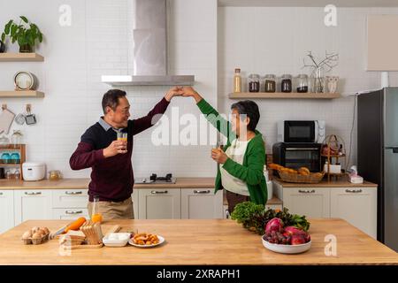 Happy senior husband and wife having fun in the kitchen utensils, cooking together at home, very glad the mature adults are there. A gray-haired, ener Stock Photo