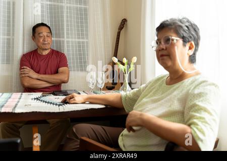 Asian senior couple having relationship problems, angry at each other sitting at the dining table, refusing to talk. Stock Photo
